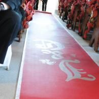 Red carpeted aisle between rows of people standing in red uniforms, with white calligraphy on the floor