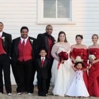 Wedding party posing outdoors in front of a white building, with bride, groom, and attendants in formal attire