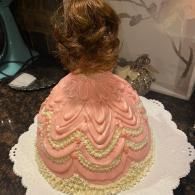 Pink frosted cake shaped like a dress on a white scalloped platter
