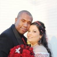 Couple posing together, holding a bouquet of red flowers, smiling at the camera.