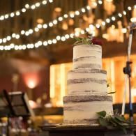 Three-tiered naked wedding cake with greenery at a warmly lit reception
