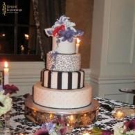 Tiered wedding cake with white and black stripes, topped with blue and purple flowers, on a decorated table
