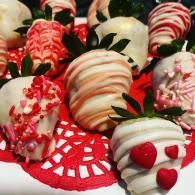 Chocolate-covered strawberries with red, white, and pink drizzles on a red doily