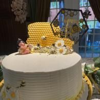 White frosted cake topped with yellow honeycomb, bees, and a decorative hive on a table in a room