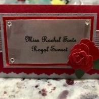 Red and silver personalized plaque with black script and red flower decorations on a speckled surface