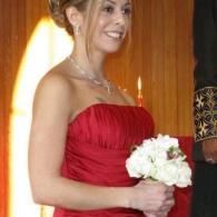 Woman in a red strapless dress holding a white bouquet, smiling indoors.