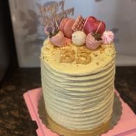 Yellow frosted birthday cake with pink macarons and gold “35” topper on a pink board
