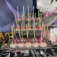 Tiered dessert display with pink cake pops and gold sprinkles on a decorated table.
