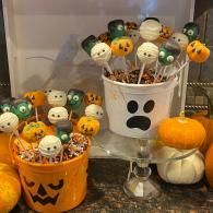 Halloween cake pops in pumpkin and ghost buckets, with mini pumpkins on a shelf.