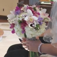 Hand holding a bouquet of white and purple flowers with green accents