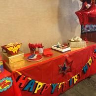Birthday party dessert table with red decorations and a colorful “Happy Birthday” banner