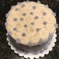 Round white frosted cake with piped rosettes and gray dots on a scalloped white cake board