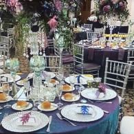 Elegant banquet table with purple tablecloth, floral centerpieces, and place settings in a decorated reception hall