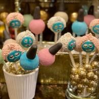 Candy-coated cake pops in blue and pink, arranged in glass jars at a festive display.