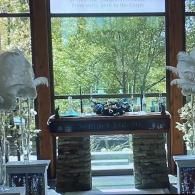 Interior view of a window with a stone table and floral arrangements, overlooking green trees outside