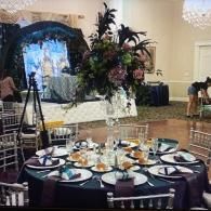Elegant banquet table with black tablecloth, gold chargers, and a floral arch centerpiece in a ballroom