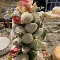 Vertical dessert display of white and pink treats arranged with flowers on a banquet table