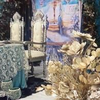 Ornate dining setup with gold chairs, patterned tablecloth, and white floral decor in a blue-toned room