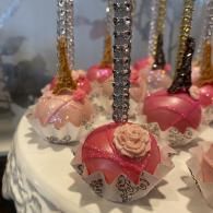 Decorated pink and gold dessert pops with jeweled sticks on a white platter