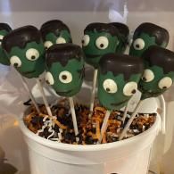 Marshmallow treats on sticks in a white bucket, decorated like green cartoon faces with googly eyes