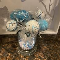 Clear vase of blue and white decorative snowballs with glittery silver stems on a countertop