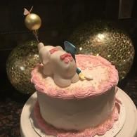 Pink frosted cake with a unicorn topper and gold balloon decoration on a white plate