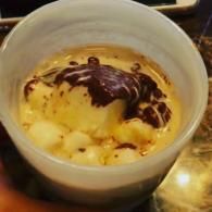 Ice cream dessert in a clear cup, topped with chocolate sauce and nuts on a table.