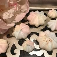 White and pale pink meringue cookies on a tray, with a large flower-like pastry at left.