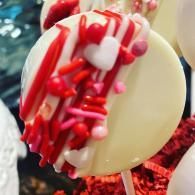 White candy pop decorated with red drizzle, sprinkles, and heart shapes on a red background