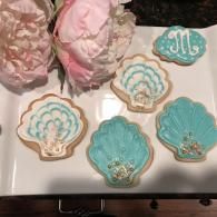 Decorated seashell-shaped cookies in pastel blue and cream with pink flowers on a white tray