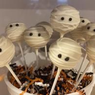 Halloween mummy cake pops in a white bowl, decorated with chocolate eyes and wrapped in orange-black sprinkles