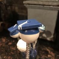 Small blue-and-white toy figure with a graduation cap on a chain against a dark background