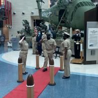 Mannequins in tan uniforms stand in a museum exhibit beside a large military vehicle.