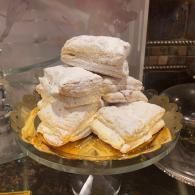 Stack of powdered sugar pastries on a glass cake stand inside a display case