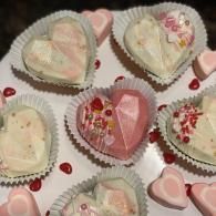 Heart-shaped pastel cookies and candies arranged in paper cups on a white surface.
