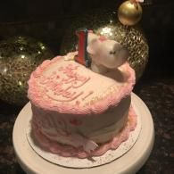 Small pink frosted birthday cake with a candle and teddy bear topper on a white plate