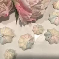Pastel pink and white flower-shaped meringues on a white surface