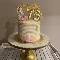 Gold-and-white 75th birthday cake on a stand with floral and bow decorations