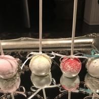 Three pastel-colored round ornaments hanging from a metal rack, dusted with frost or glitter