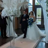 Bride walking down a mirrored aisle with a man, holding a blue bouquet, in a decorated indoor venue