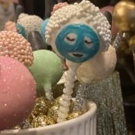 Decorated cake pops with pastel coatings, including a blue face design and white candy sprinkles