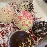 Assorted decorated chocolate truffles in a white box, with pink, white, and dark chocolate drizzles