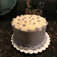 White frosted cake with purple icing accents on a scalloped white cake board