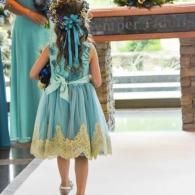 Girl in a turquoise dress with braided hair walking outdoors toward a doorway