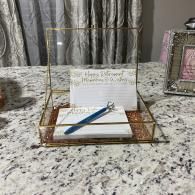 Guestbook and pen on a marble countertop beside a framed photo and curtains.