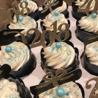 Rows of cupcake-like desserts with white frosting, blue accents, and gold number toppers on a table
