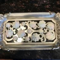 Silver tray with ornate cutout floral design holding pastel flower-shaped candies on a dark surface