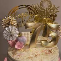 Gold 75th birthday cake topper with gold and white floral decorations on a frosted cake