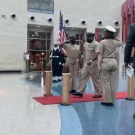 Uniformed officers stand at attention indoors beside an American flag during a ceremony.