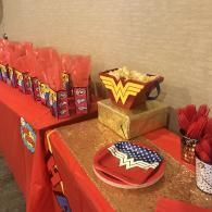 Wonder Woman-themed party table with red decorations, plates, and snacks on a beige tablecloth